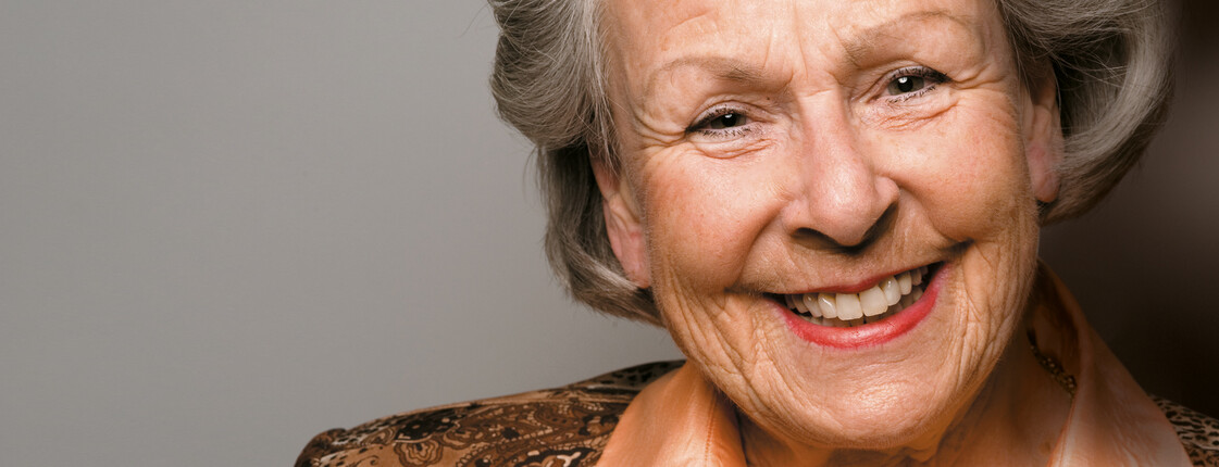 Eine ältere Dame, die schick gekleidet ist, lächelt in die Kamera.