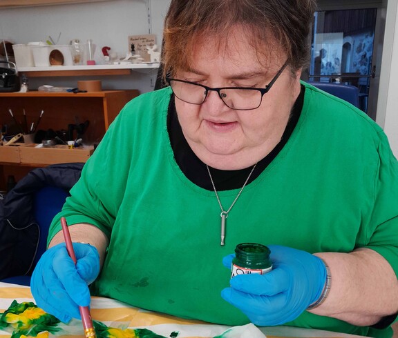 Frau in grünem Pulli bemalt einen Seidenschal