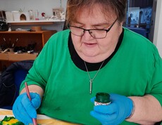 Frau in grünem Pulli bemalt einen Seidenschal