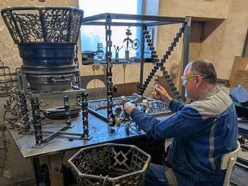 Mann von hinten rechts im Bild sitz am Tisch und arbeitet mit Metallteilen.