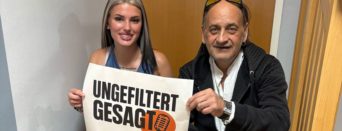 Natalie und Sigi sitzen auf Treppen mit einem Schild "ungefiltert gesagt"