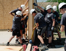 SChüler*innen im Arbeiteroutfit helfen zusammen um eine Holzwand aufzustellen