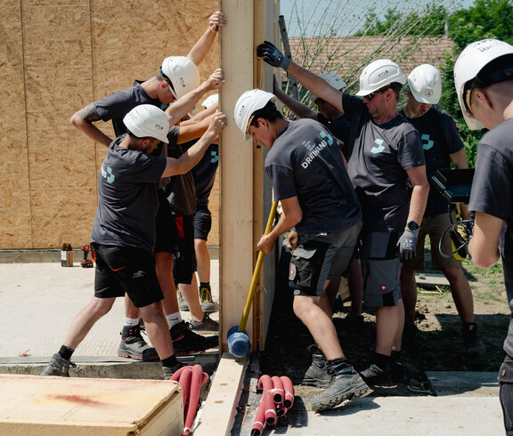 SChüler*innen im Arbeiteroutfit helfen zusammen um eine Holzwand aufzustellen