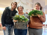 Drei Frauen schauen in die Kamera, die beiden rechts und in der Mitte halten je einen Adventkranz in die Höhe.