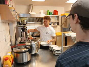 Ein Mann schöpft Suppe aus einem großen Topf in einen Suppenteller