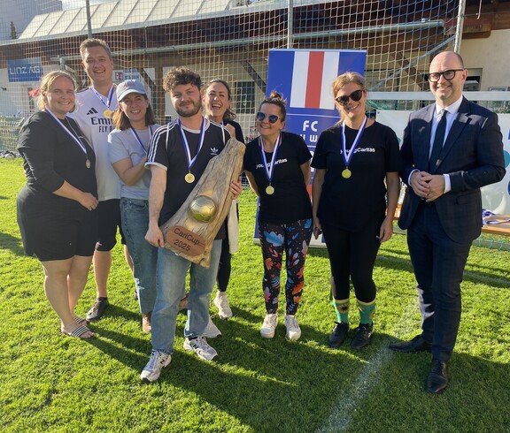 Sechs Personen stehen am Spielfeld und ein Mann hält den Pokal in den Händen.