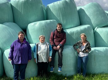 Vier Personen stehen vor einer Mauer aus silierten Heuballen.