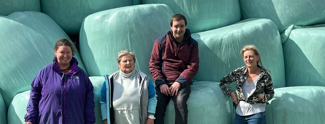 Vier Personen stehen vor einer Mauer aus silierten Heuballen.