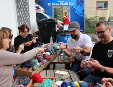 Drei Personen sitzen im Freien und versuchen sich beim Häckeln.