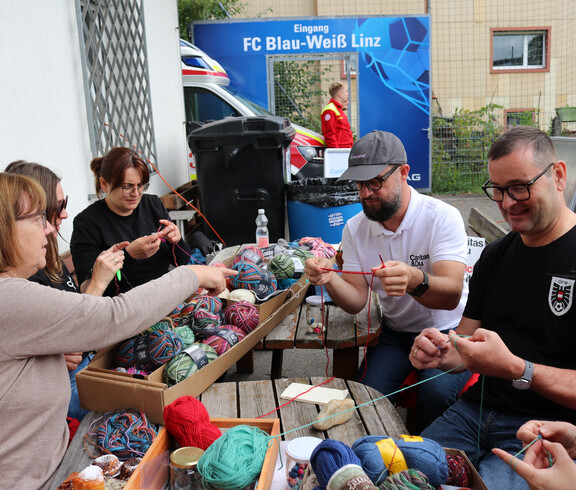 Drei Personen sitzen im Freien und versuchen sich beim Häckeln.