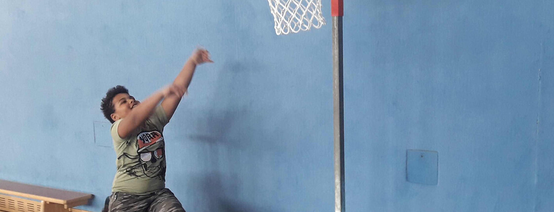 ein Bub sitzt in einem Rollstuhl und wirft einen Ball in den Basketballkorb