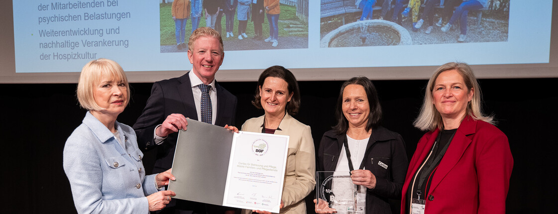 Fünf Personen stehen auf einer Bühne und halten eine Urkunde in den Händen.