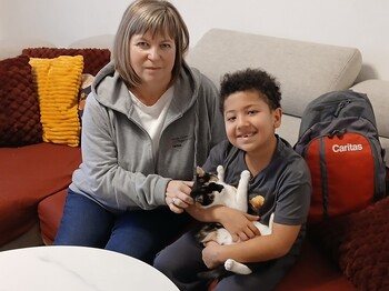 Frau sitzt mit Bub auf Sofa. Bub hat Katze am Arm.