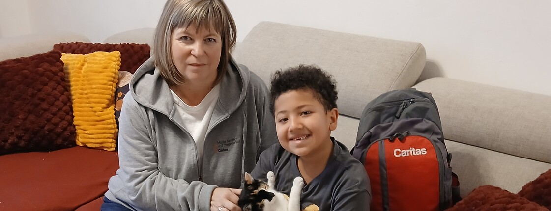 Frau sitzt mit Bub auf Sofa. Bub hat Katze am Arm.