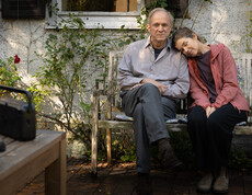 Frau lehnt an der Schulter ihres Mannes, sie sitzen im Garten 