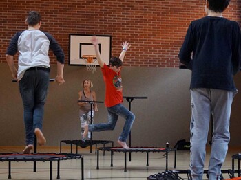 Kinder springen in einem Turnsaal auf Trampolin herum. 