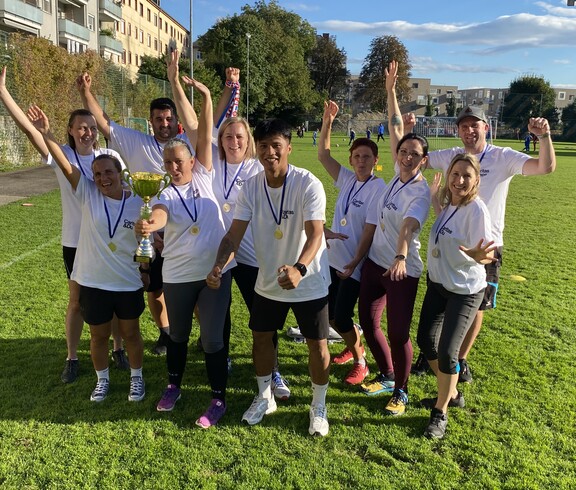 10 Personen in weißen Caritas-T-Shirts und Medaillien stehen am Spielfeld und freuen sich.