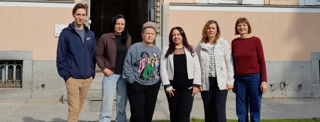 Sechs Personen stehen in einer Reihe vor einem Haus und schauen in die Kamera