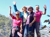 Vier Personen stehen in Wanderkleidung im Freien und winken.