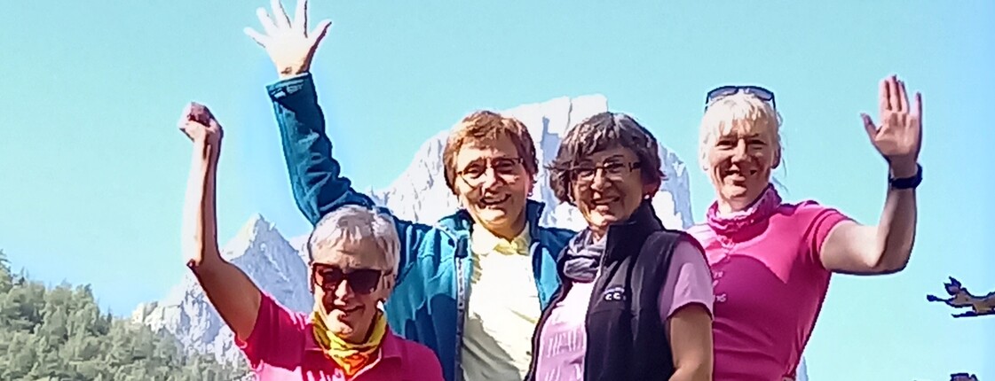 Vier Personen stehen in Wanderkleidung im Freien und winken.