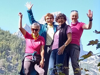 Vier Personen stehen in Wanderkleidung im Freien und winken.