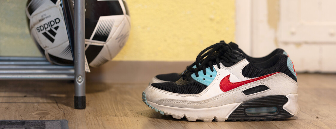 In einem Hauseingang stehen ein Paar Sneaker und ein Fußball liegt auch einem Schuhregal.