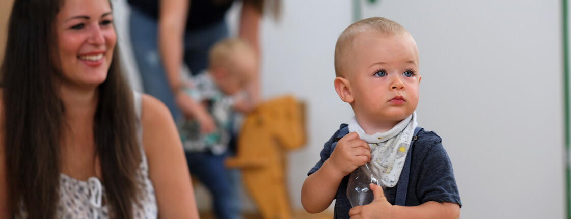 Eine Mutter mit Kleinkind, das eine Flasche in den Händen hält, bei einem Mutter-Kind-Kurs.