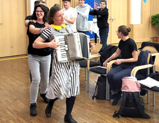 Frau mit Zieharmonika tanzt mit Menschenschlange durch den Saal