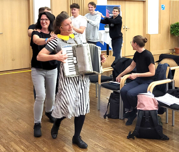 Frau mit Zieharmonika tanzt mit Menschenschlange durch den Saal
