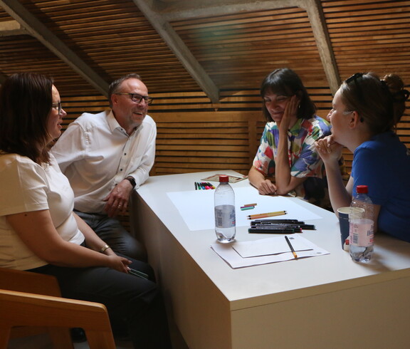 Vier Personen besprechen etwas und sitzen rund um einen Tisch.