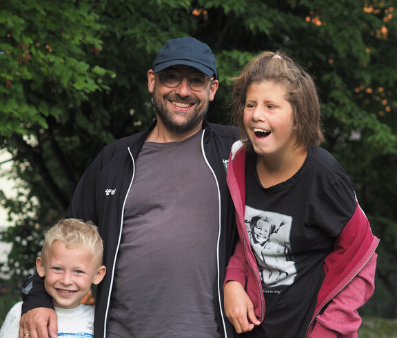 Ein Mann mit Kappe und zwei Kindern, alle lachen.