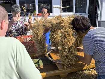 Eine Erntekrone steht im Freien auf einem Biertisch und wird noch von einer Frau geschmückt.