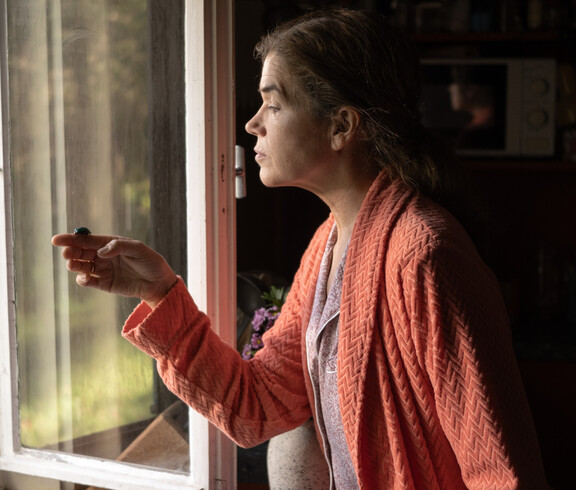 Frau steht vor offenem Fenster und hat kleinen Käfer in der Hand