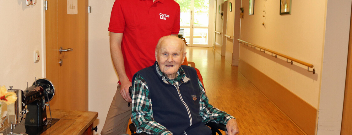 Zivildiener Jakob Osterberger schiebt den 87-jährigen Ludwig Humer im Rollstuhl.