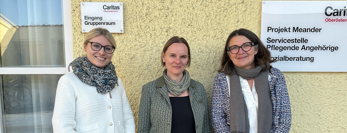 Drei Frauen stehen vor einer gelben Hauswand und lächeln in die Kamera