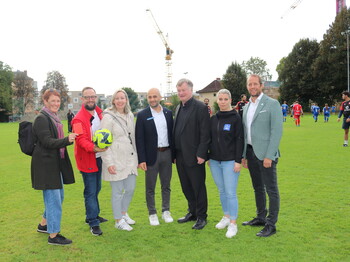 Sieben Personen stehen auf einem Fussballfeld im Freien.