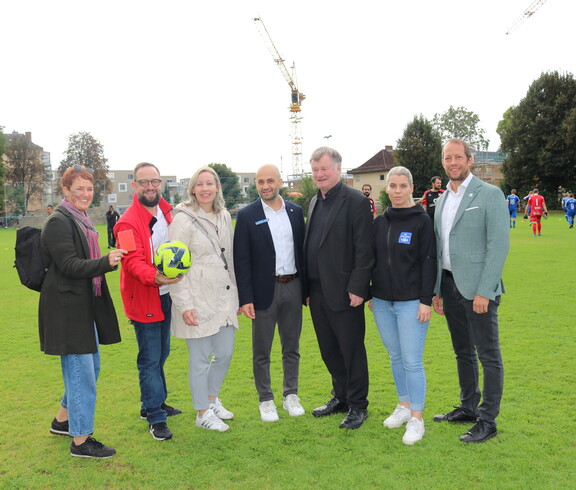 Sieben Personen stehen auf einem Fussballfeld im Freien.