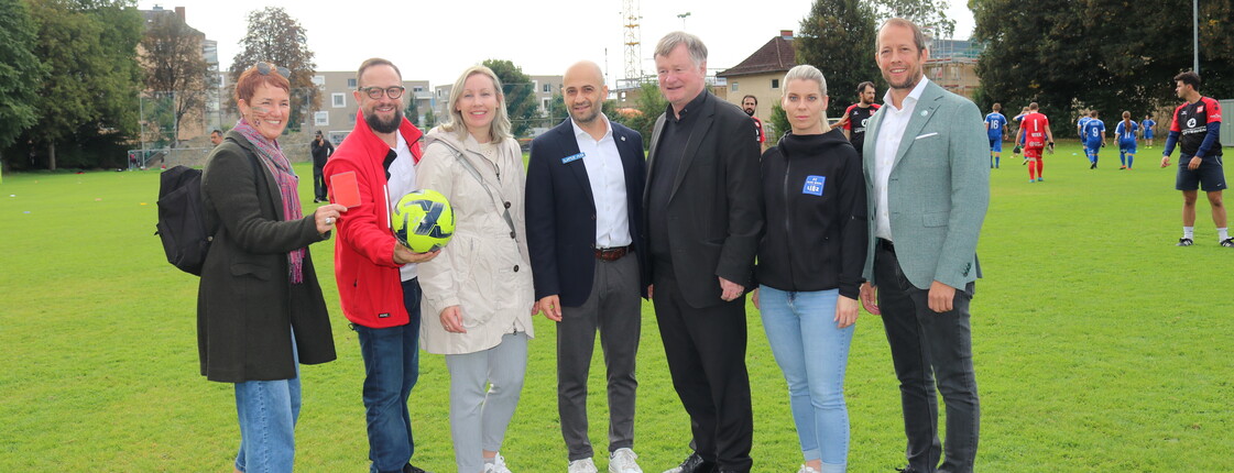 Sieben Personen stehen auf einem Fussballfeld im Freien.