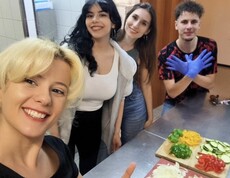 Fünf Menschen stehen um einen Arbeitsplatz in der Küche. Geschnittenes Gemüse und ein großer Topf sind zu sehen.