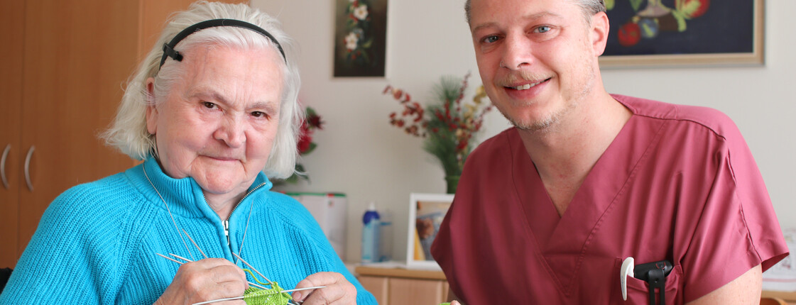 Ein Pfleger strickt mit einer Seniorin.