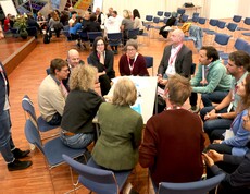 Blick auf eine Gruppe von Personen, die rund um einen Tisch sitzen und sich unterhalten.