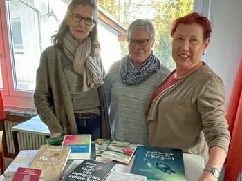 Drei Frauen stehen hinter einem Tisch auf dem Bücher liegen.
