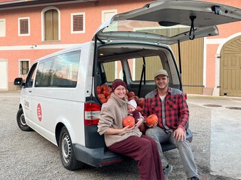 Frau und ein Mann sitzen mit Banby im offenen Kofferaum von einem Kleinbus und halten Kürbisse in der Hand