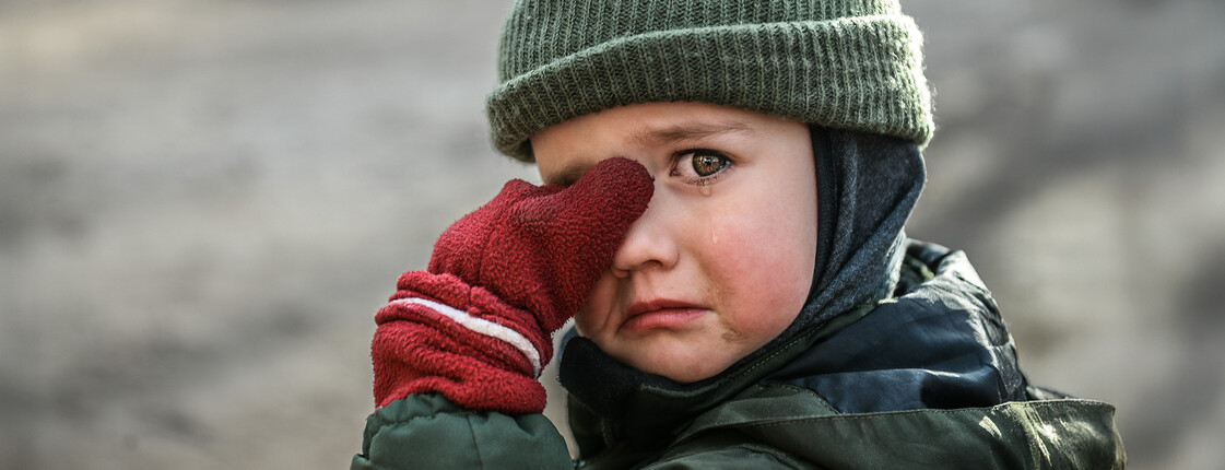 Kind mit Mütze und roten Handschuhen wischt sich weinend die Augen ab