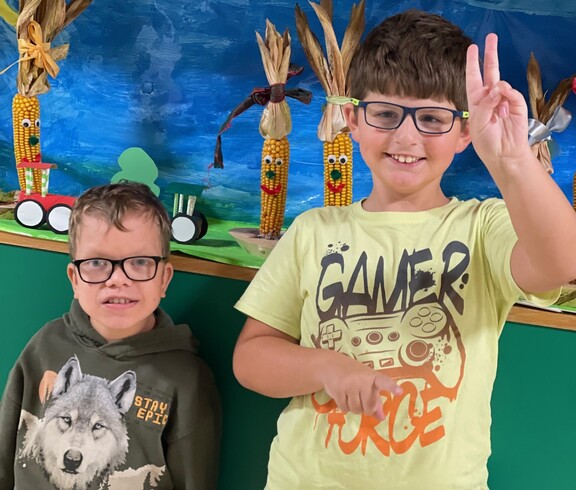 Zwei Jungs stehen nebeneinander, einer von ihnen macht das Peace Zeichen und grinst in die Kamera