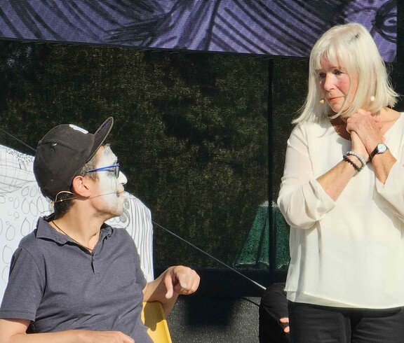Mann mit weißer Gesichtsbemalung auf einer Bühne mit einer Frau im weißen Shirt.