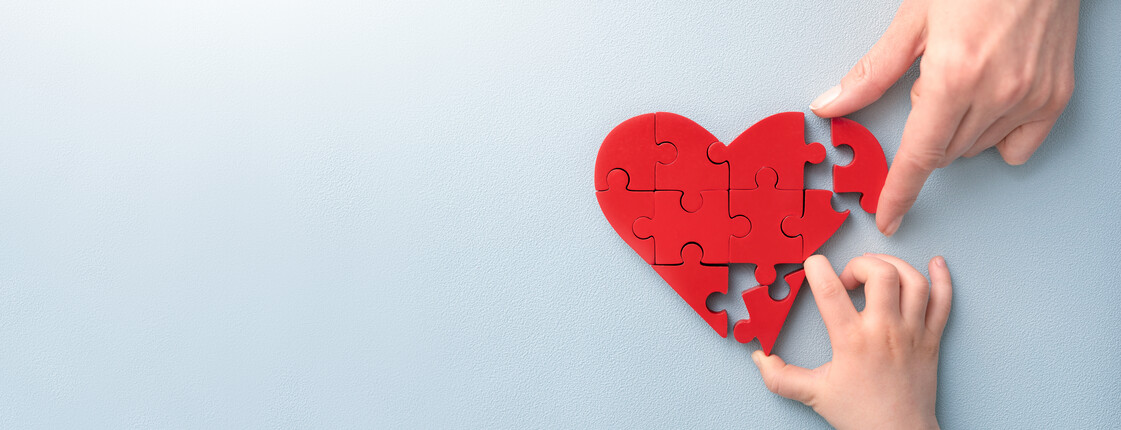 Eine Frauen- u. eine Kinderhand fügen ein herzförmiges Puzzle zusammen. 