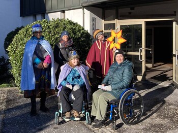 Drei Sternsinger mit Begleitung, zwei Personen im Rollstuhl.