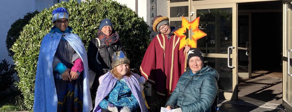 Drei Sternsinger mit Begleitung, zwei Personen im Rollstuhl.