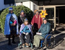 Drei Sternsinger mit Begleitung, zwei Personen im Rollstuhl.